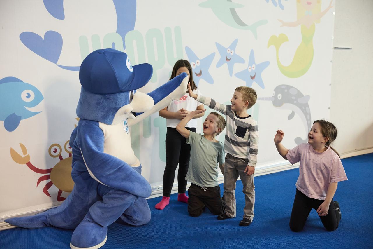 Eine Gruppe Kinder mit dem Maskottchen Flosse macht High Five