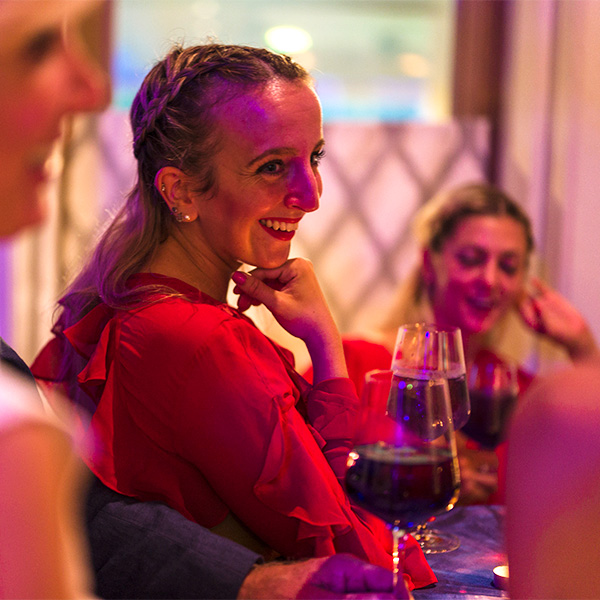 Glückliche Frau mit einem Glas Rotwein an der Bar in Gesellschaft