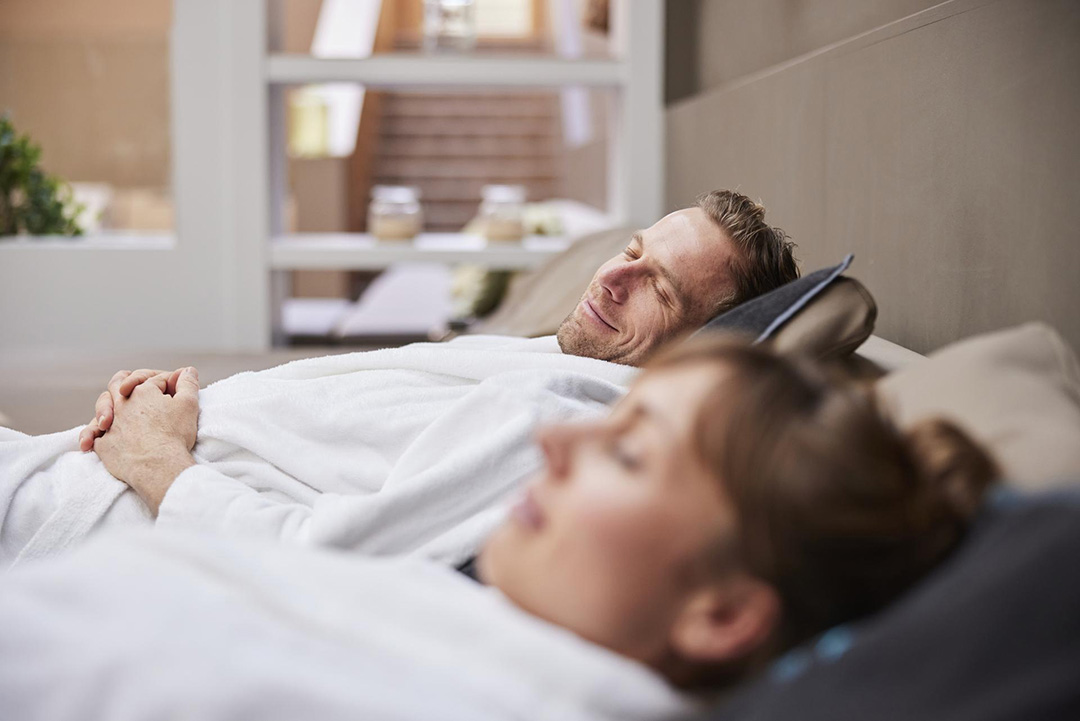 Mann und Frau die im Bademantel auf den Liegen im Wellnessbereich entspannen