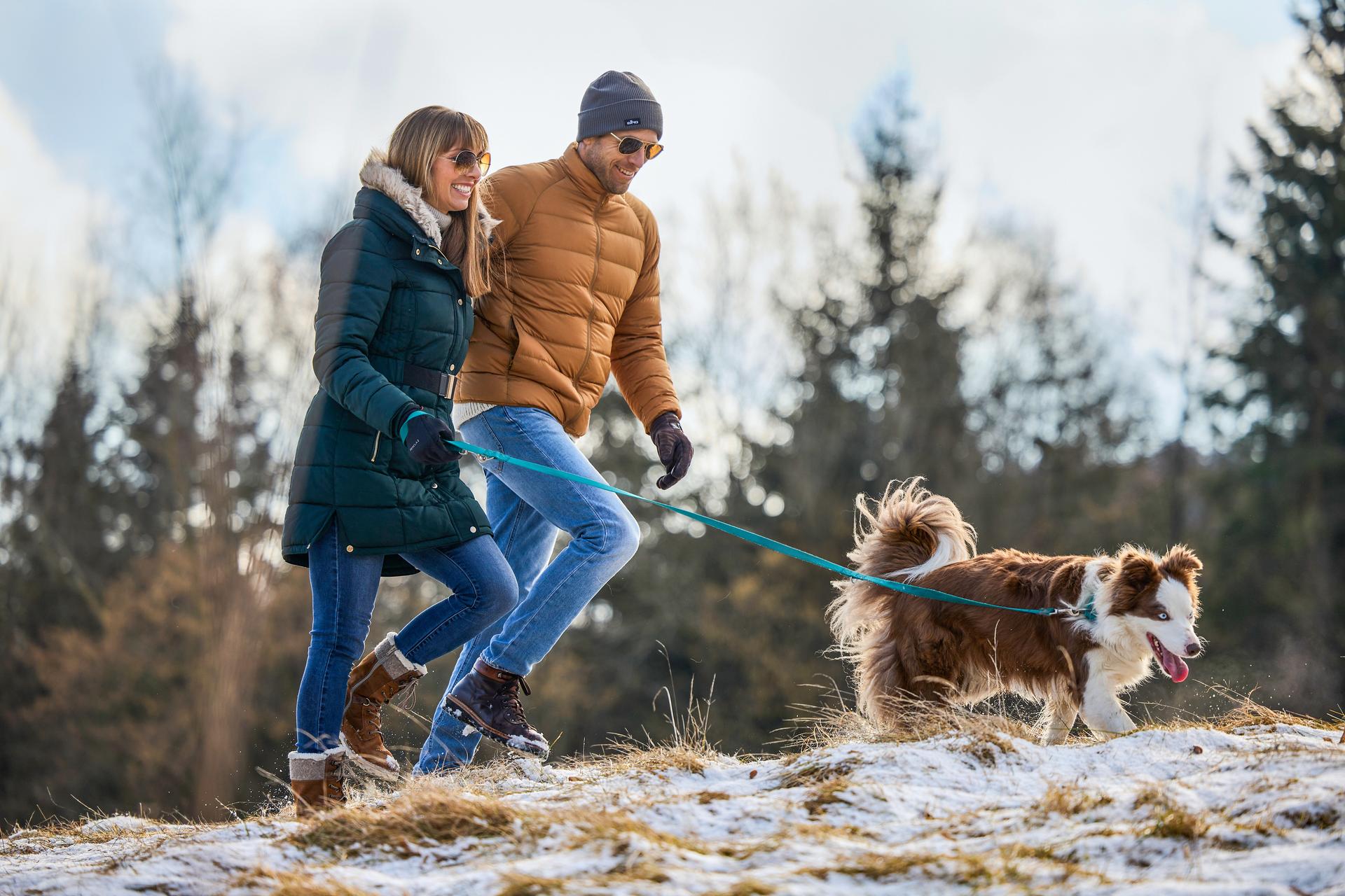 Frau und Mann spazieren mit ihren Hund durch den verschneiten Hausruckwald